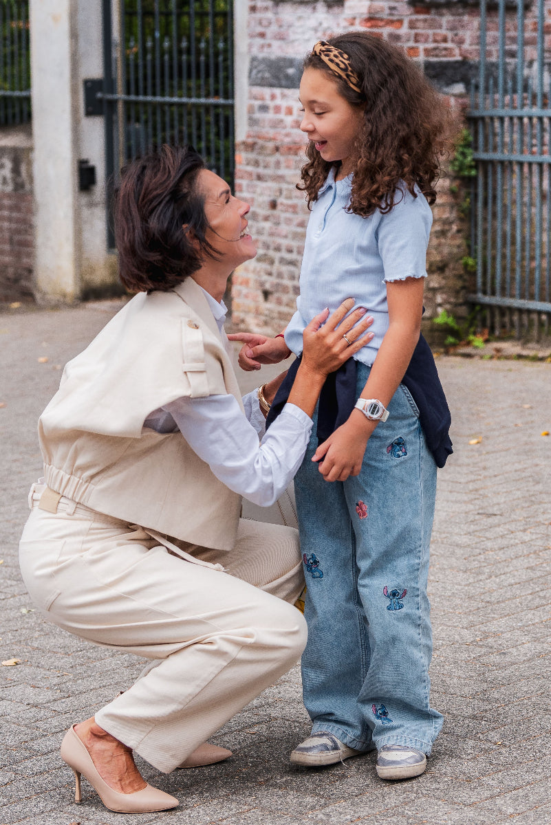 Woman in beige outfit kneeling down to interact with a child in a blue outfit on a street.