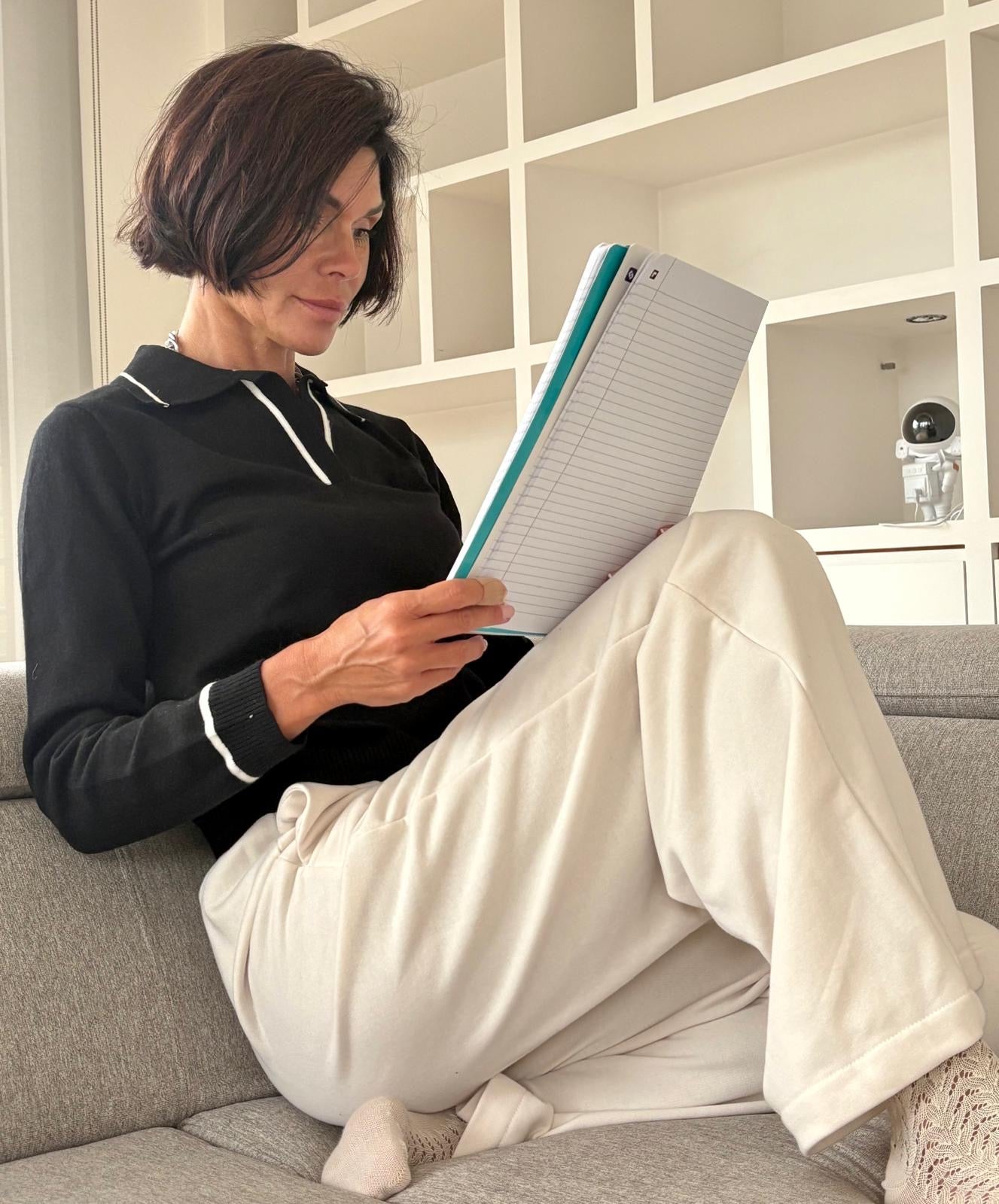 Woman sitting on a couch reading a book in a cozy living room.