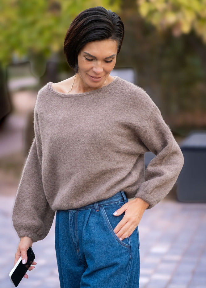 Woman wearing a gray sweater and blue jeans walking outdoors.