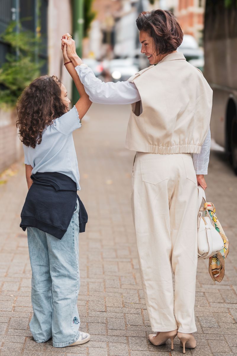 Woman and child on a street, woman in beige outfit with child in light blue shirt and jeans.