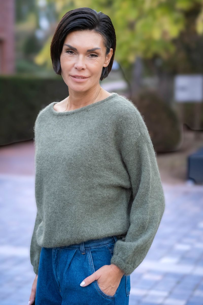 Woman wearing a green sweater and blue jeans standing outdoors.