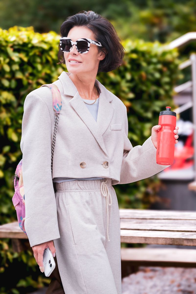 Woman in light gray coat holding a red water bottle outdoors