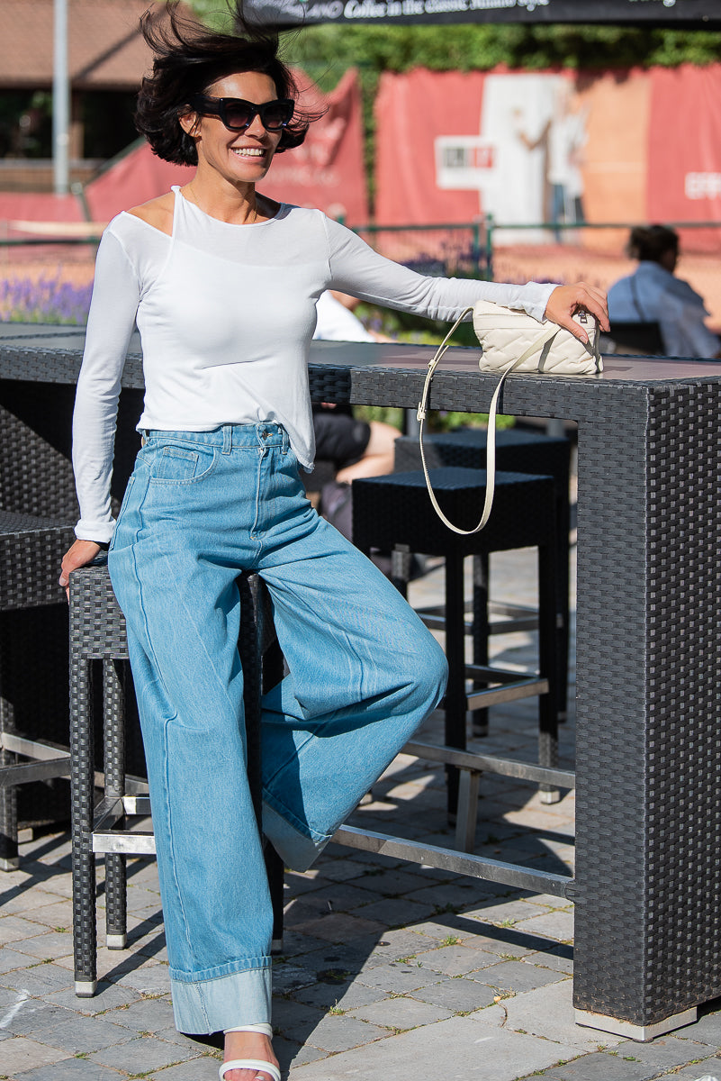Woman in white top and blue jeans sitting at an outdoor cafe table.